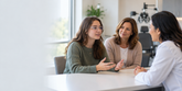 Illustrative consultation with a young adult wearing glasses, an eye care clinician and a supportive parent.