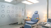 A softly lit pediatric eye examination room with a child-sized chair in the foreground and a blurred vision chart in the background, evoking clinical precision and pediatric vision testing.