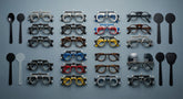 An organized flat-lay arrangement of various trial frame sizes and occluder accessories on a clean clinical surface, representing optometric refraction tools for diverse patient populations.